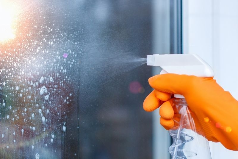 Person using an orange cleaning globe spraying Windex to a glass window